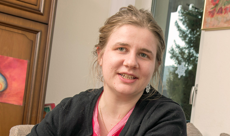 Eine Frau sitzt drinnen und blickt freundlich in die Kamera.